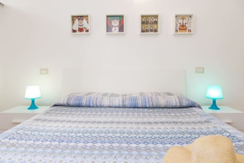 Bright bedroom at Agriturismo Chiai Francesco with blue striped bedding, turquoise lamps, and four framed artworks on white