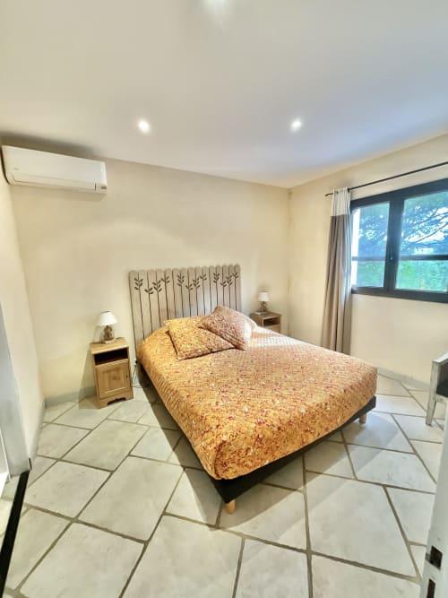 Chambre spacieuse à la Domaine Pero Longo à Sartène avec lit queen-size, tables de nuit en bois et grandes fenêtres donnant sur le jardin