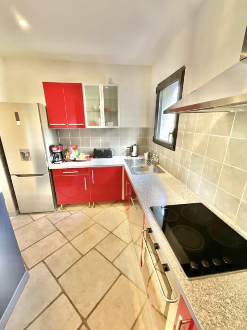 Cuisine moderne de l'Appartement Bavella au Domaine Pero Longo à Sarténe, avec armoires rouges, électroménagers inox et carrelage