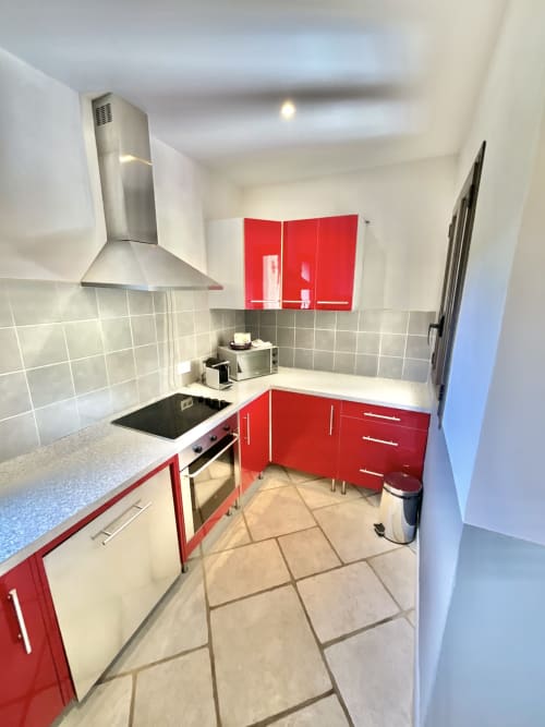 Cuisine moderne avec armoires rouges, appareils en acier inoxydable et dosseret en carrelage gris à l'appartement Domaine Pero Longo