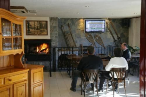 Sala de estar del Hotel Llibrada en Benasque con chimenea, muebles de madera e invitados en las mesas