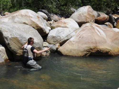 Pescador de mosca vadea un arroyo entre grandes rocas cerca del Hotel Llibrada en Benasque