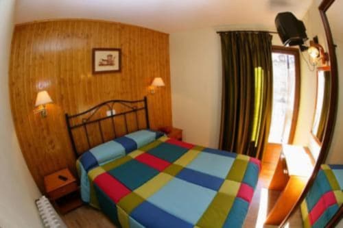 Dormitorio colorido en Hotel Llibrada de Benasque con paneles de madera, colcha estampada y luz natural