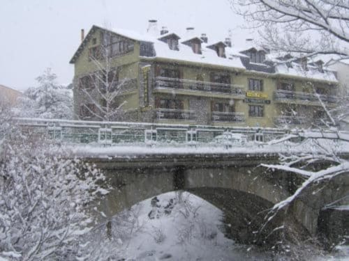 Hotel Llibrada en Benasque en invierno, edificio de piedra amarilla con tejado nevado frente a un puente congelado