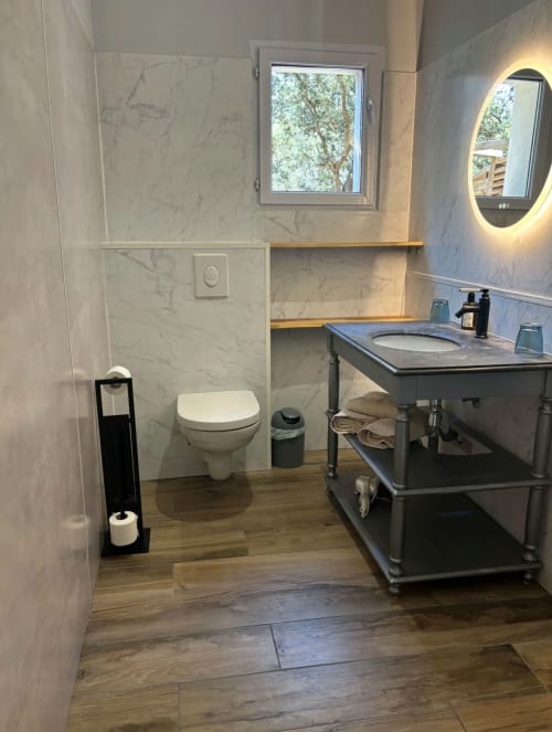 Salle de bain moderne au Domaine Pero Longo à Sartène avec murs en marbre, vasque, toilettes et parquet