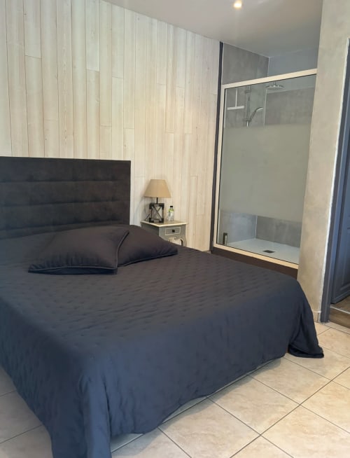 Chambre Ortolo au Domaine Pero Longo à Sartène avec lit sombre, salle de douche attenante et panneaux muraux en bois clair