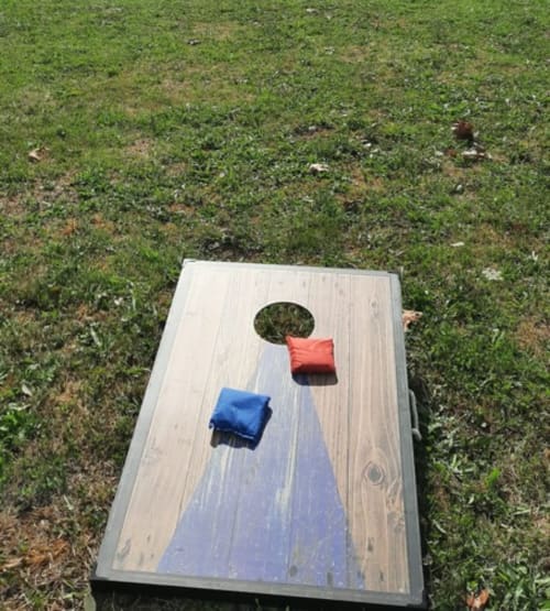 Jeu de cornhole avec sacs de haricots bleus et rouges sur l'herbe à Home Sweet Lodge Glamping Aquitaine