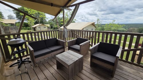 Terrasse ombragée avec salon de détente en bois, table basse et vue panoramique sur la campagne à Home Sweet Lodge glamping,