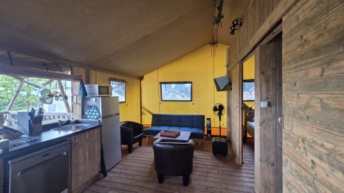 Intérieur lumineux d'un cottage de glamping jaune vif à Home Sweet Lodge Aquitaine avec cuisine, canapé bleu et mobilier en bois