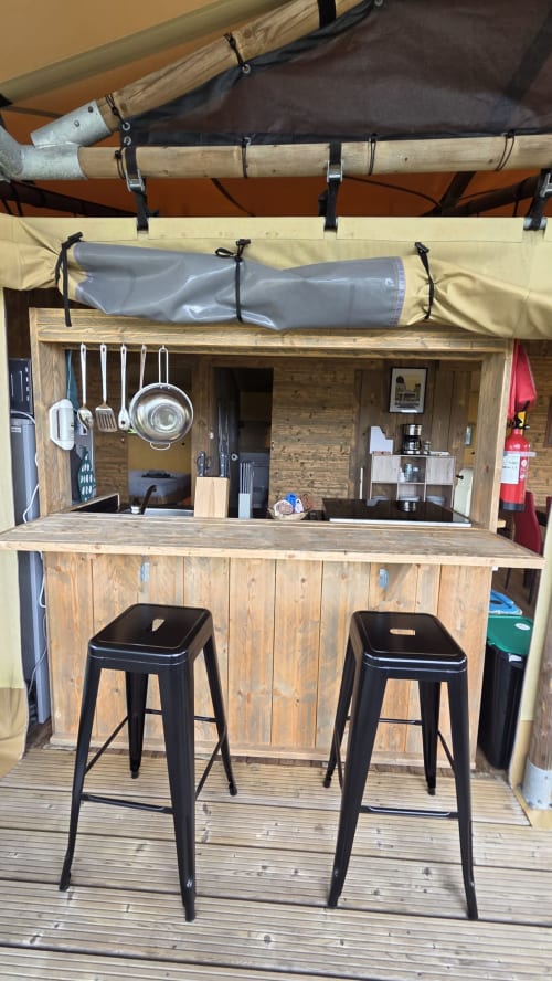 Comptoir de cuisine glamping en bois rustique avec tabourets noirs, ustensiles suspendus et kitchenette équipée à Home Sweet Lodge
