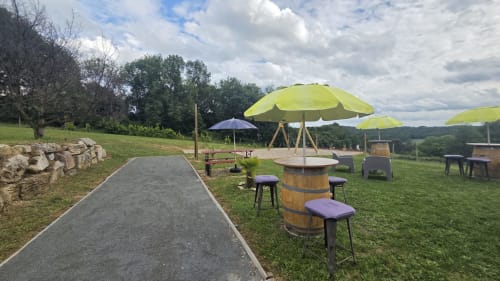 Espace détente extérieur du Home Sweet Lodge Glamping avec tables en tonneau, parasols citron vert et vues sur la campagne vallonnée d'Aquitaine