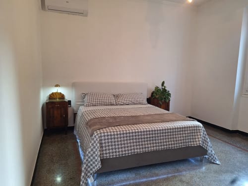 Camera moderna alle Kate Apartments Genova con biancheria a quadri, comodino in legno, pianta in vaso e vista sulla città