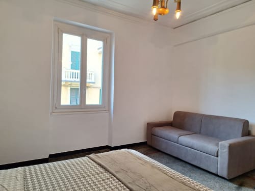 Ampio soggiorno ad Kate Apartments Genova con divano grigio, tappeto decorativo e vista sulla città dalle finestre francesi