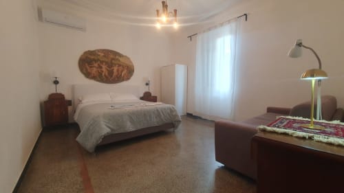 Ampia camera da letto in Kate Apartments Genova con letto matrimoniale, divano e vista città attraverso tende trasparenti