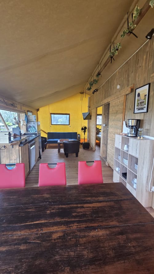 Spacieux intérieur de cottage glamping à Home Sweet Lodge Aquitaine avec murs jaunes, sièges roses, cuisine équipée et