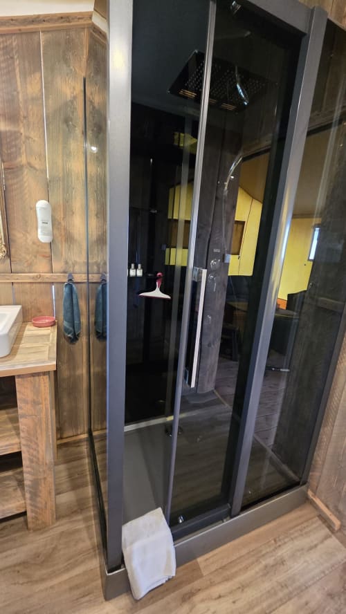 Paroi de douche au cadre noir moderne dans la salle de bain du gîte glamping Home Sweet Lodge, avec finitions en bois et équipements