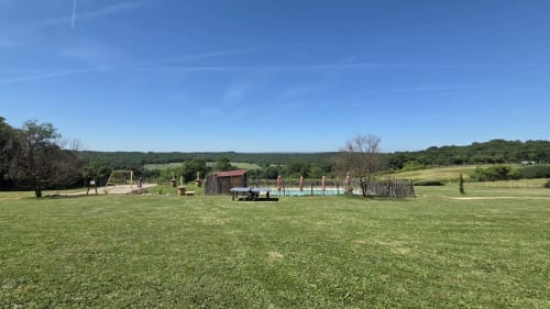 Vaste pelouse verte avec équipements de jeux pour enfants et paysage rural à Home Sweet Lodge Glamping en Aquitaine