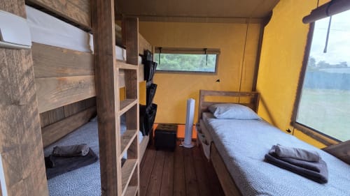 Helder gele glamping tent interieur met stapelbedden en eenpersoonsbed met uitzicht op het meer bij Home Sweet Lodge Aquitaine
