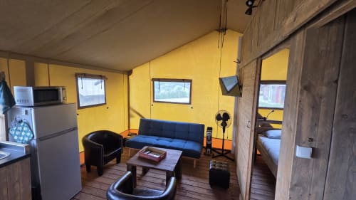 Interieur van gele glamping tent met blauwe bank, zwarte stoelen en houten accenten bij Home Sweet Lodge Aquitaine