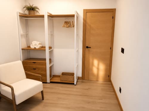 Moderno dormitorio de apartamento con armario, puerta de madera y silla color crema en Alojamientos Apoio 360, Caldas de Reis