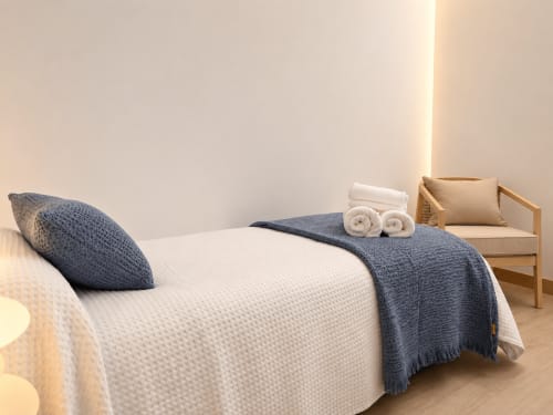 Dormitorio moderno en Apoio 360 de Caldas de Reis con cama blanca, almohadas azules, toallas enrolladas y silla de madera