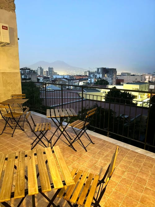 Rooftop terrace at Neapolis Tecnotourist B&B with wooden chairs, city skyline and mountains view in Naples, Italy