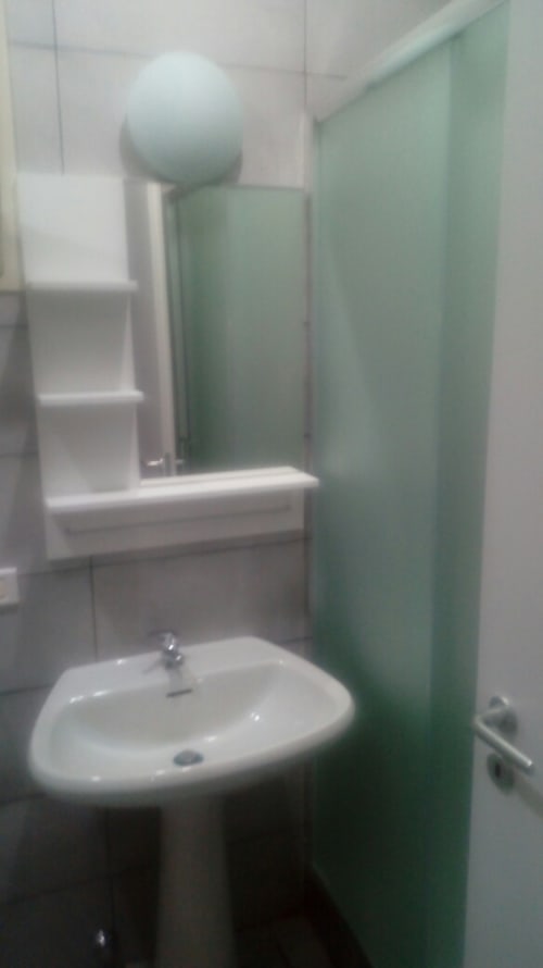 Modern bathroom in Italian apartment with white sink, green shower enclosure, and white tile walls