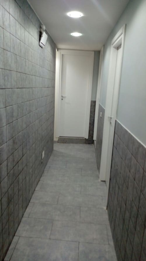 Modern hallway in Neapolis Tecnotourist apartment with gray tile walls, recessed lighting, and white doors leading to rooms