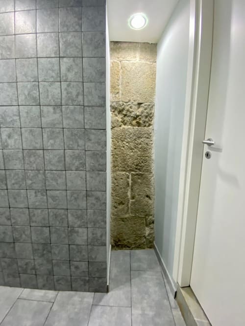 Modern bathroom shower with gray tiles and stone accent wall at Neapolis Tecnotourist BnB in Italy