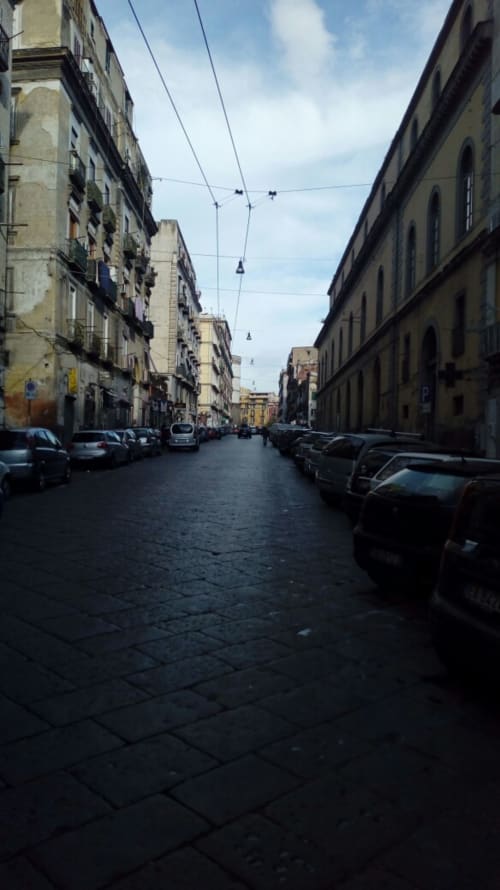 Neapolis street in Italy with historic buildings, parked cars, and overhead trolley wires