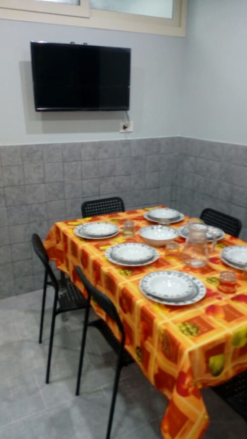 Dining area in Neapolis Tecnotourist apartment with colorful tablecloth, place settings, and wall-mounted TV