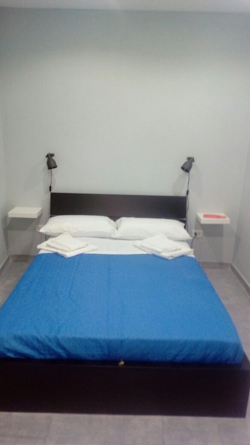 Bedroom at Neapolis Tecnotourist B&B with blue comforter, white pillows, black headboard, and white nightstands