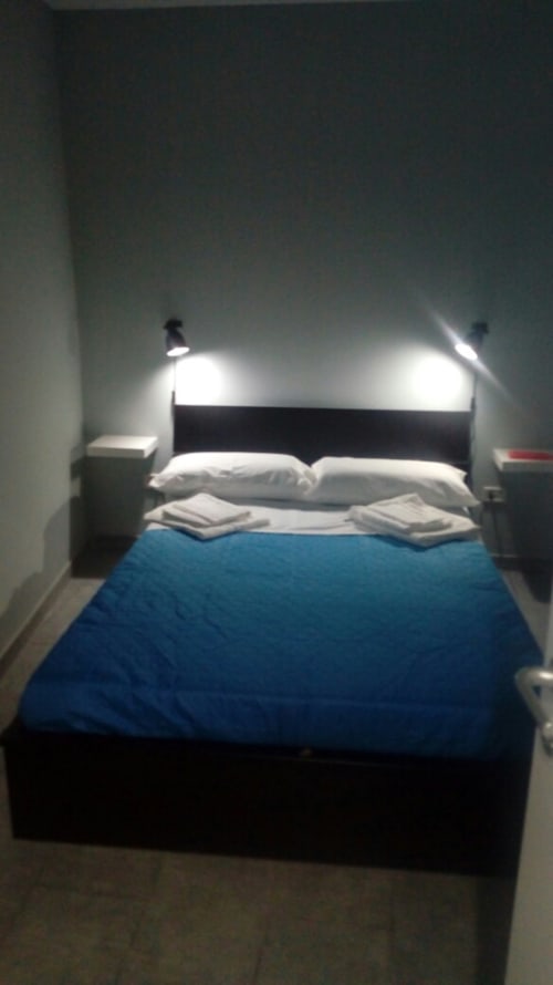 Modern bedroom with blue comforter, white pillows, black bed frame, and wall-mounted lights at Neapolis Tecnotourist BnB in