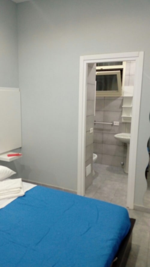 Bedroom with blue comforter and open bathroom door showing toilet and shelving at Neapolis Tecnotourist apartment, Italy