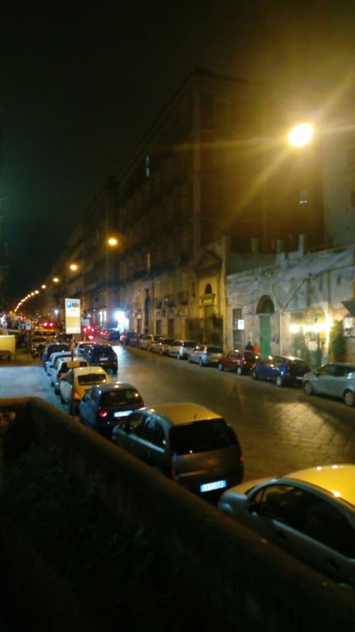Evening street view of Neapolis Tecnotourist B&B in Naples, Italy with parked cars and historic buildings illuminated by