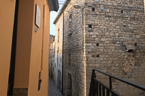 Stretto vicolo in ciottolato a Valle Mosso con edifici in pietra e muri giallo ocra, vista dall'appartamento Torre del Borgo