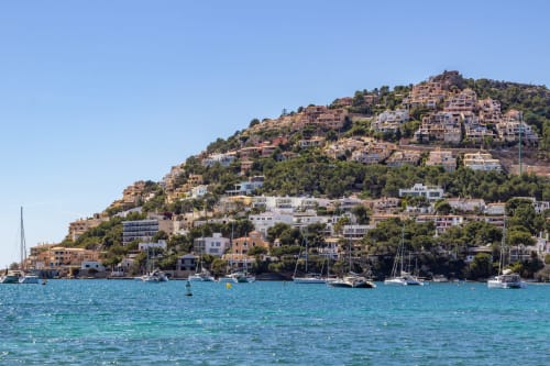 Coloridas casas en la ladera y veleros en la bahía turquesa de Paguera, España