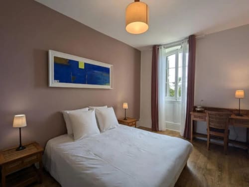 Chambre moderne à la Domaine du Faure à Chadurie avec lit blanc, murs violets et portes-fenêtres vitrées.