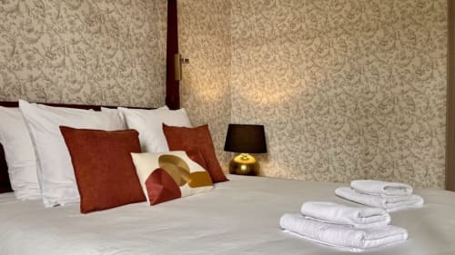 Chambre élégante au Domaine du Faure avec papier peint à motifs, accents bordeaux, lampe dorée et serviettes blanches fraîches