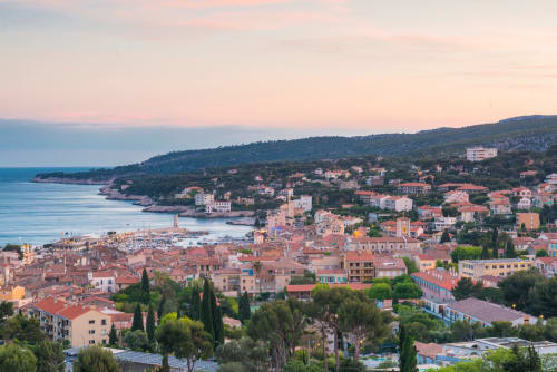 Vue aérienne au coucher de soleil d'une ville côtière méditerranéenne avec ses maisons aux toits rouges, le port et les demeures sur la colline près de Peypin