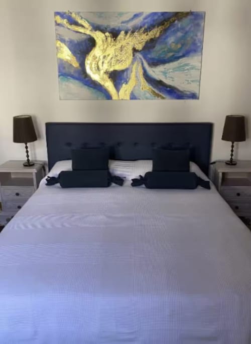 Camera moderna con testata blu navy, biancheria bianca, lampade nere e opera astratta giallo-blu a Casa Mia Vacanza
