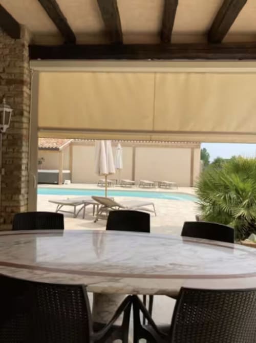 Area pranzo patio Casa Mia Vacanza con vista sulla piscina, sedie nere e tenda da sole beige retrattile