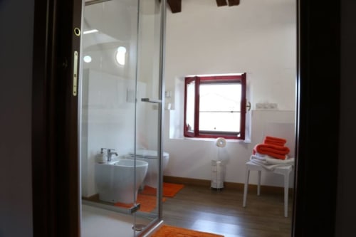 Bagno moderno a Casa Mia Vacanza con doccia in vetro, toilet, dettagli rossi e finestra nella camera Loft Arancione