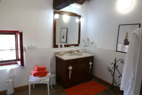 Bagno moderno di Casa Mia Vacanza con vanità in legno scuro, specchio incorniciato, asciugamani rossi e illuminazione calda