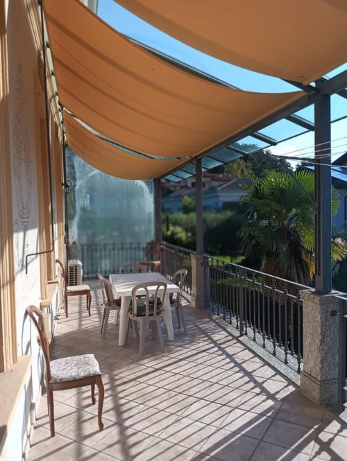 Terrazza Mia Experience con zona salotto ombreggiata, tavolo, sedie, piante di palma e vista su Monza