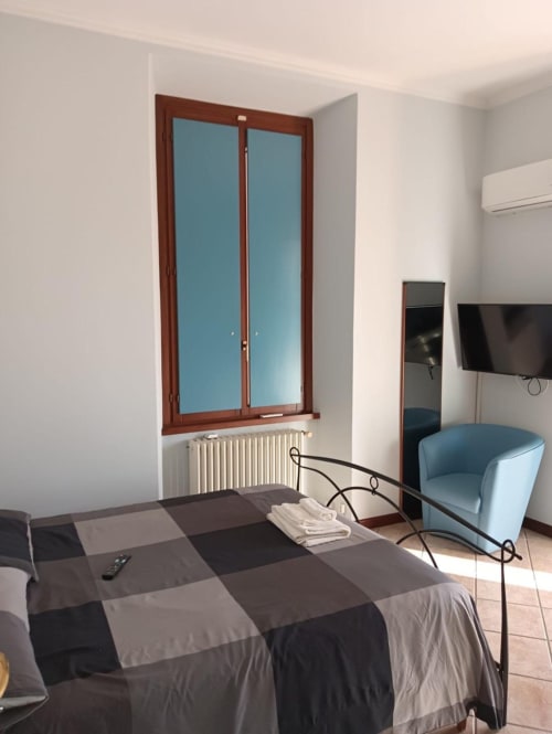 Camera Stella presso Mia Experience, Monza: letto con biancheria a quadri, poltrona blu, finestra in legno, radiatore, TV a parete