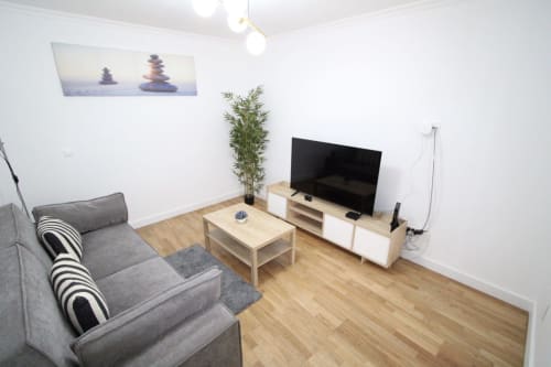 Sala de estar moderna con asientos grises, televisor de pantalla plana, muebles de madera y planta de bambú en villa de Funchal.