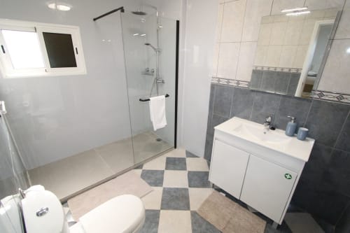 Baño moderno en la villa Atlantic Escape 2 de SpecialStays Funchal con ducha abierta, tocador blanco y piso a cuadros.