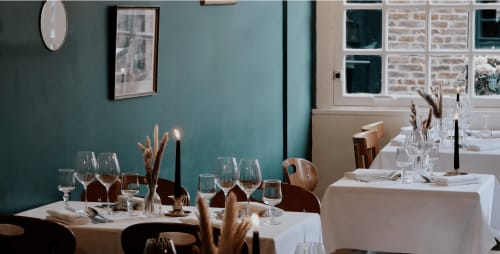 Elegant dining room at Les Maisons de Pierre et Valérie in Honfleur with teal walls, white table linens, and place settings.