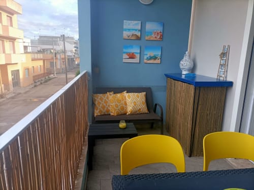 Area lounge del balcone di Le Case di Esteca con parete blu, sedie gialle, divano, decorazioni nautiche e vista sulla città